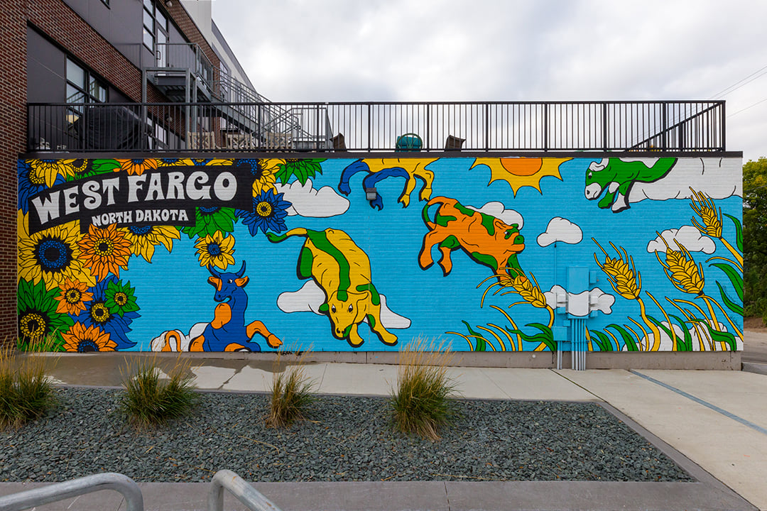 Cowtown mural located along Sheyenne Street in West Fargo, ND, featuring colorful painted cattle, sunflowers and sweet corn