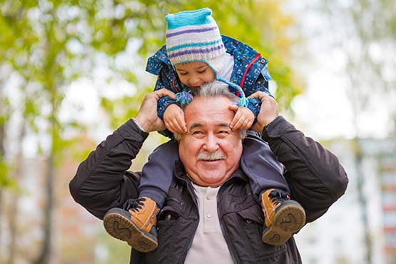 Young boy in a knitted hat, smiling and sitting on his grandpa's shoulders in Park River, North Dakota