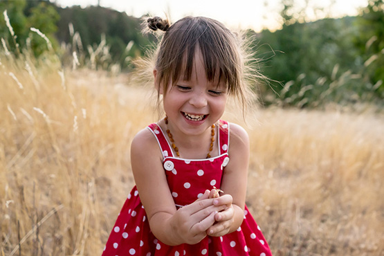 Happy little girl with pigtails in a red polka dot dress, playing in a sunny wheat field in rural North Dakota