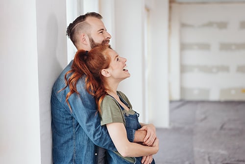 laughing redhead embraces her husband while looking at their living room under renovation