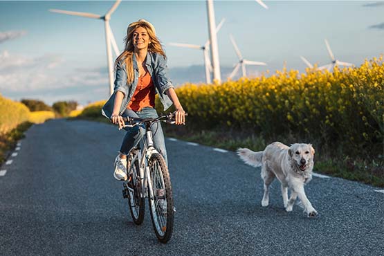 a woman rides her bike next to her dog near wind turbines after reading Gate City Bank’s tips for going green & saving money